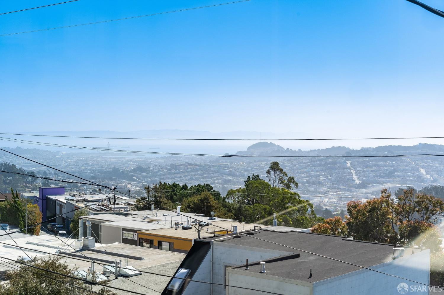Panoramic city and bay view from a hillside, with rooftops and distant hills.