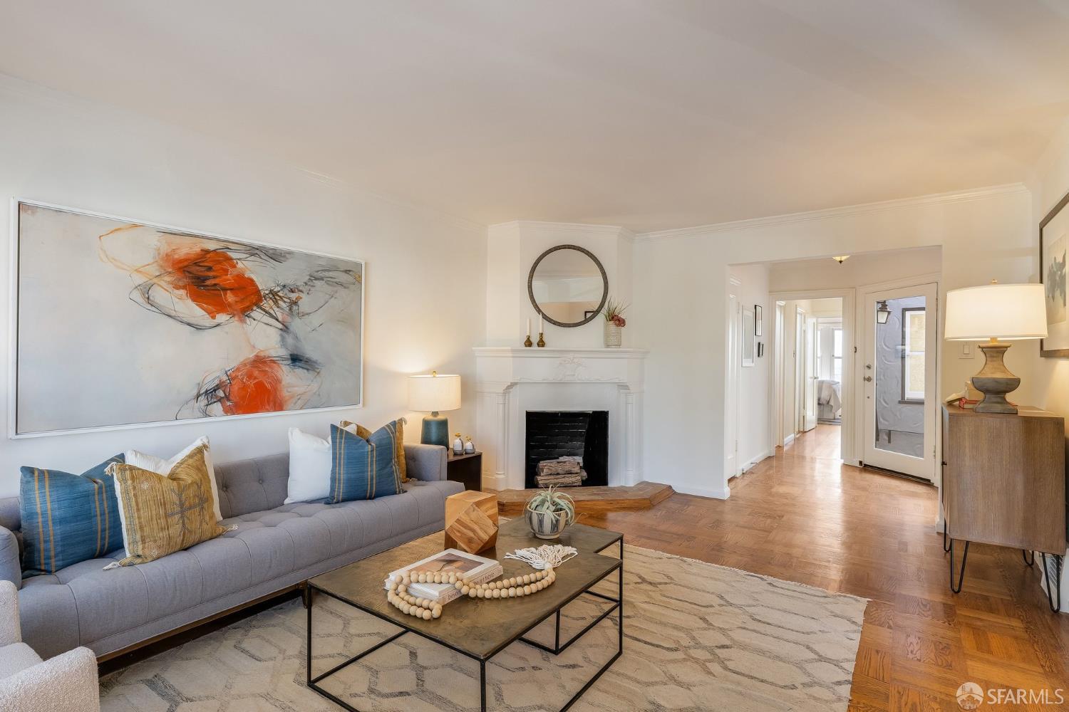 Living room with a white fireplace, gray sofa, abstract artwork, and hardwood floors.