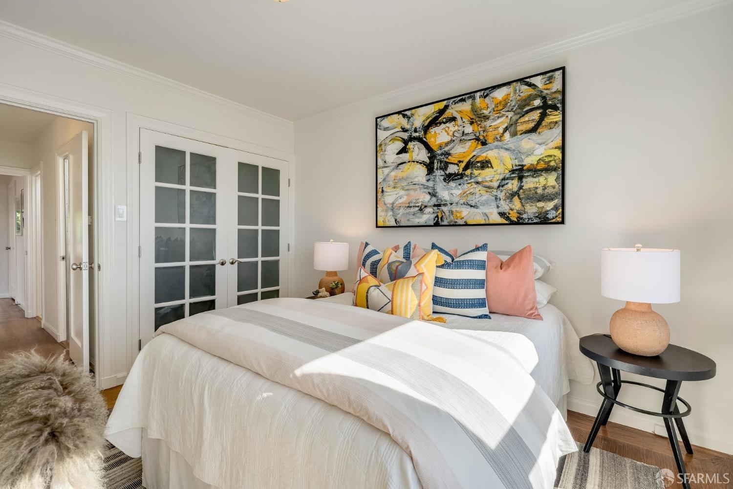 Staged bedroom with colorful pillows, glass-paneled double doors, and a large abstract painting.
