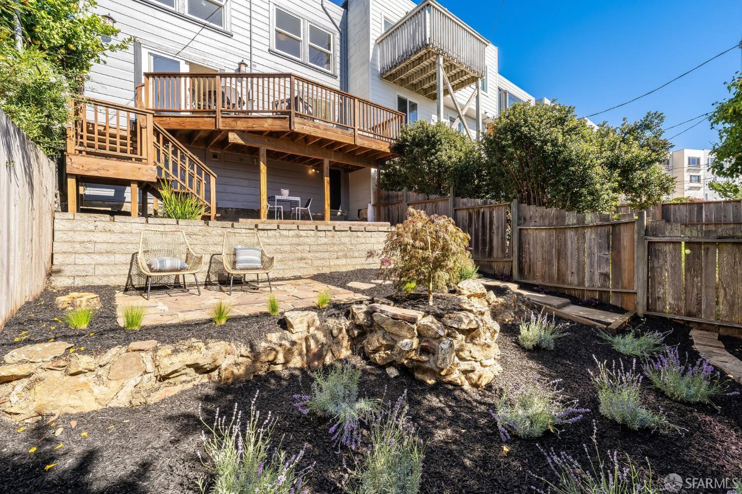 Backyard with elevated wooden decks, a stone patio, and landscaped garden beds.