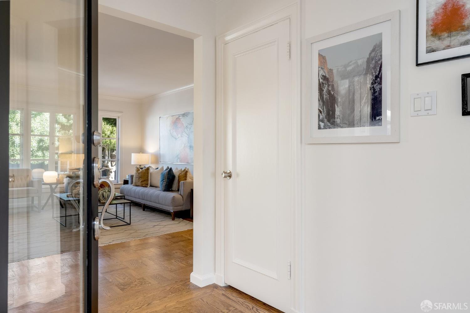 Furnished living room seen through a glass entry door, with a gray sofa and hardwood floors.