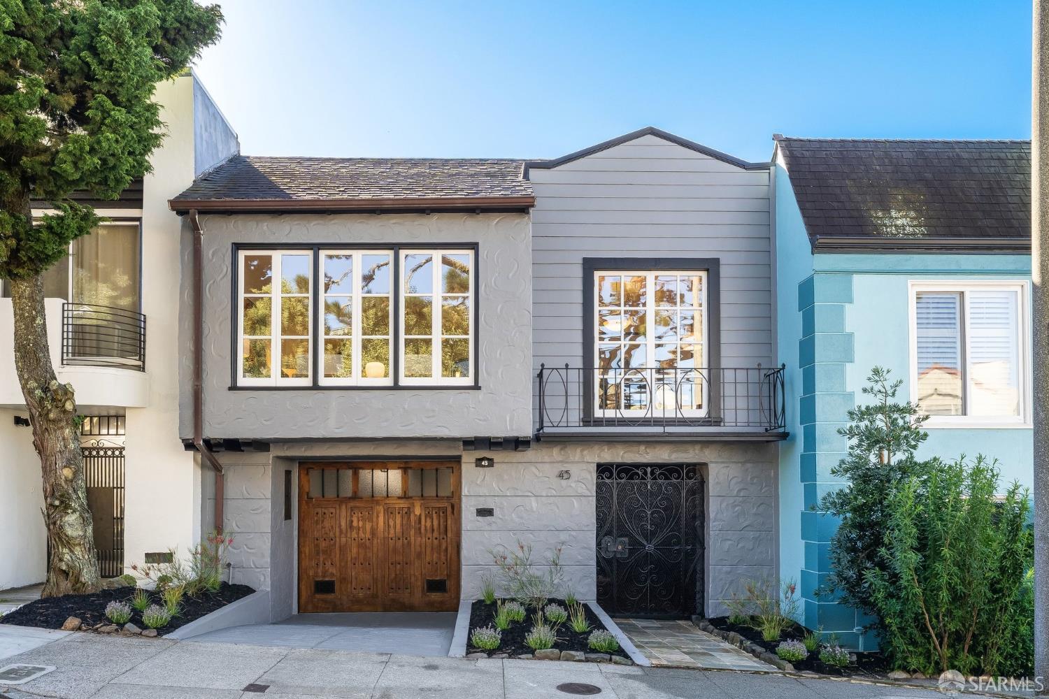 Gray two-story home with a wooden garage door, wrought-iron gate, and small upper balcony.