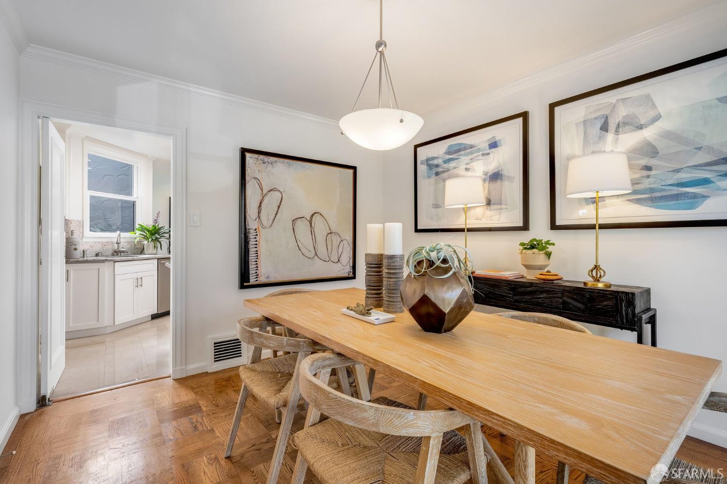 Dining room with a long wood table and woven chairs, parquet floors, and a doorway to the kitchen.