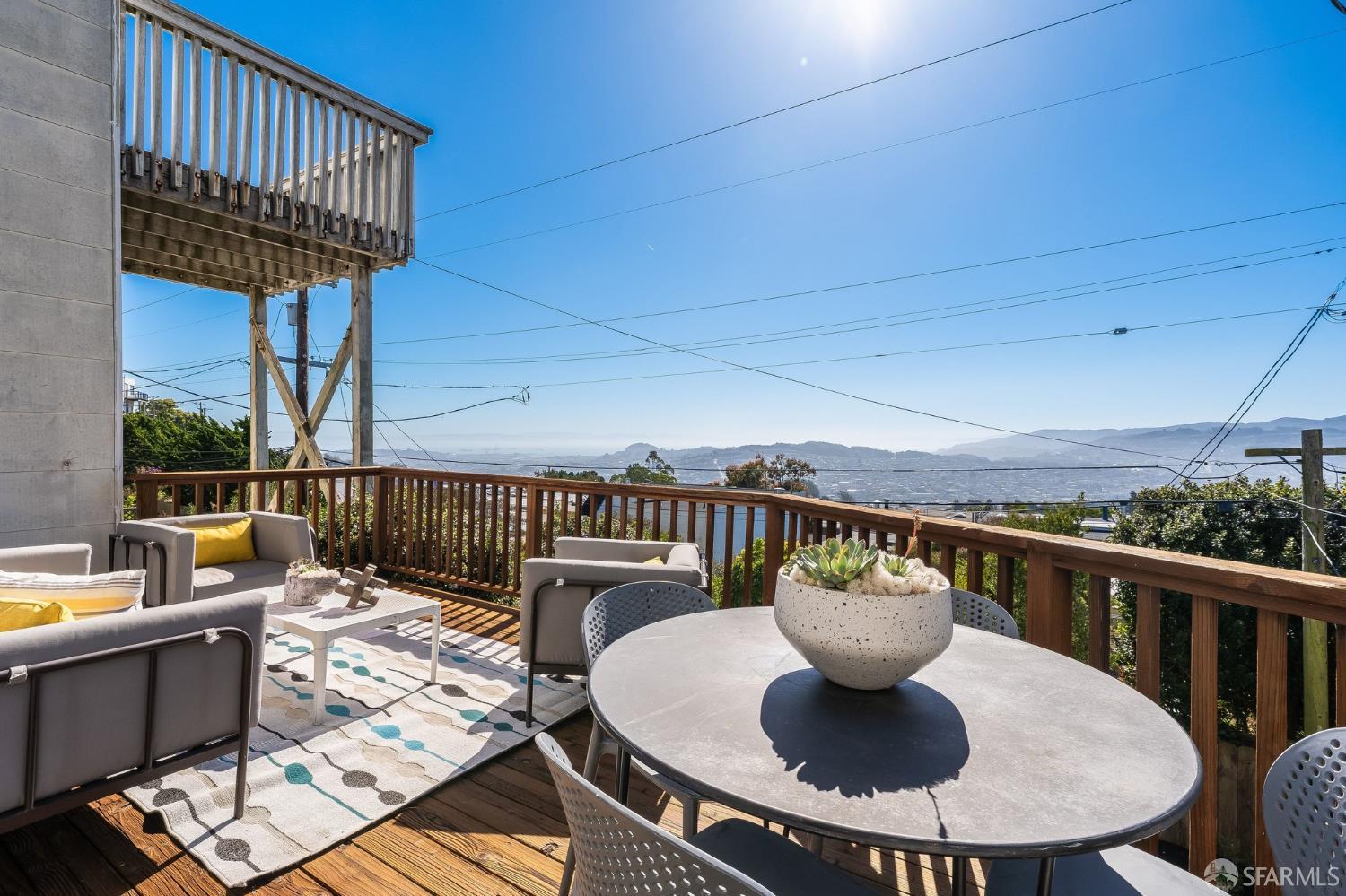 Furnished wood deck with outdoor seating and a round table overlooking distant city hills.
