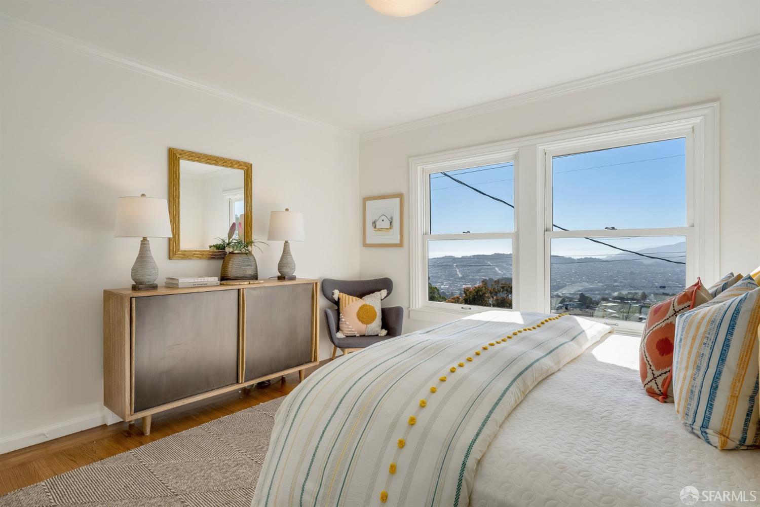 Furnished bedroom with striped bedding and large windows overlooking San Francisco.
