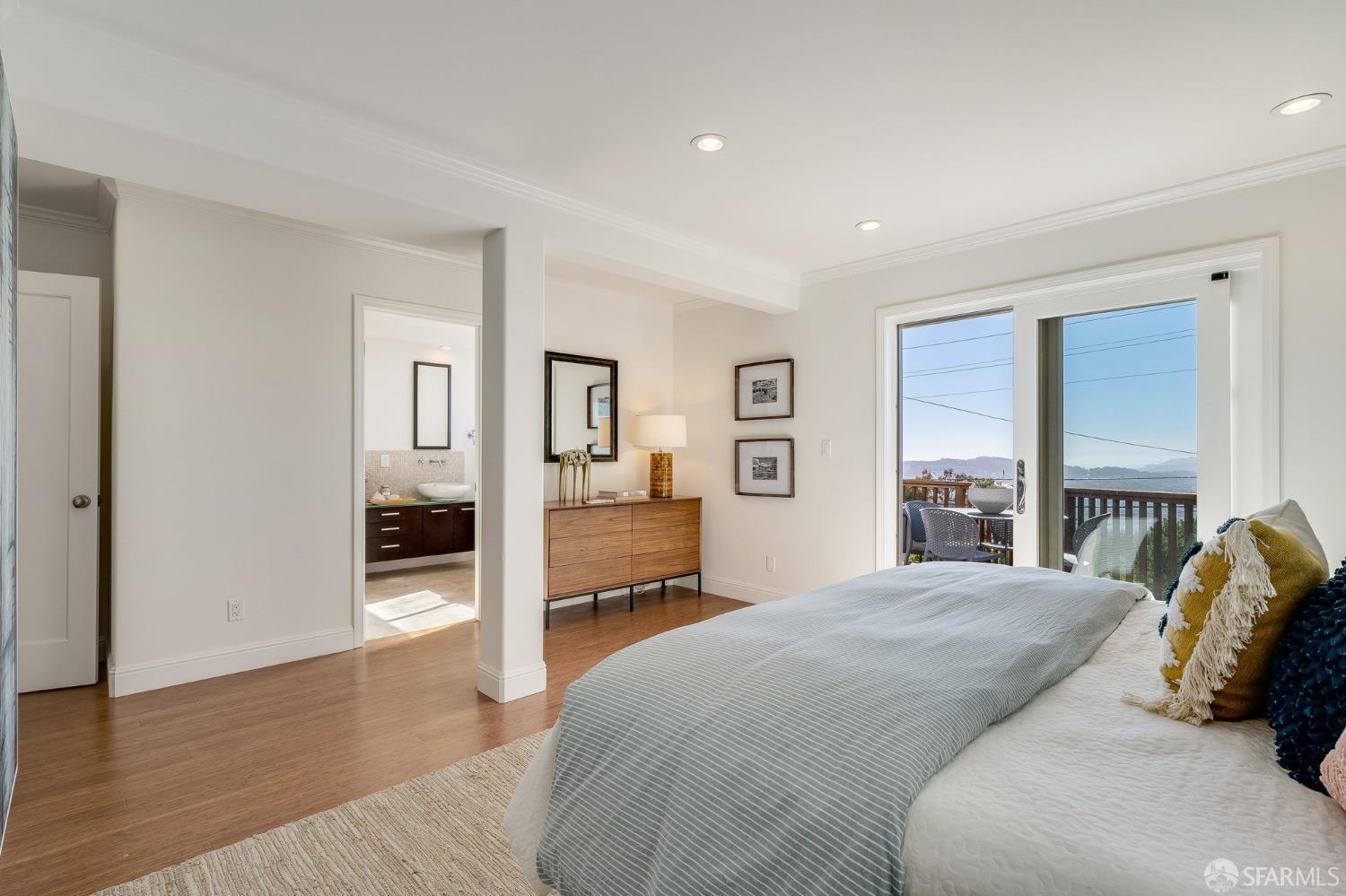 Bedroom with a large bed and sliding doors opening onto a balcony with distant hill views.