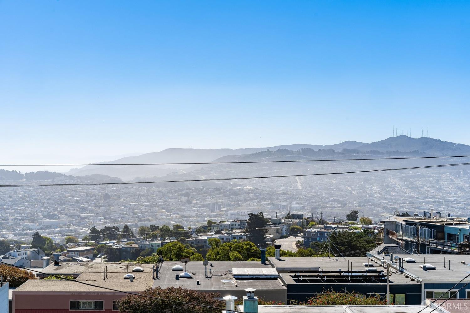 City and hillside views over San Francisco rooftops beneath a clear blue sky.