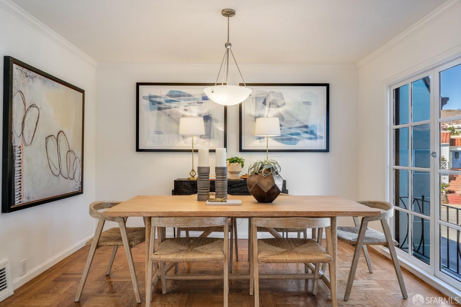 Dining room with a light wood table, woven chairs, abstract artwork, and tall divided windows.