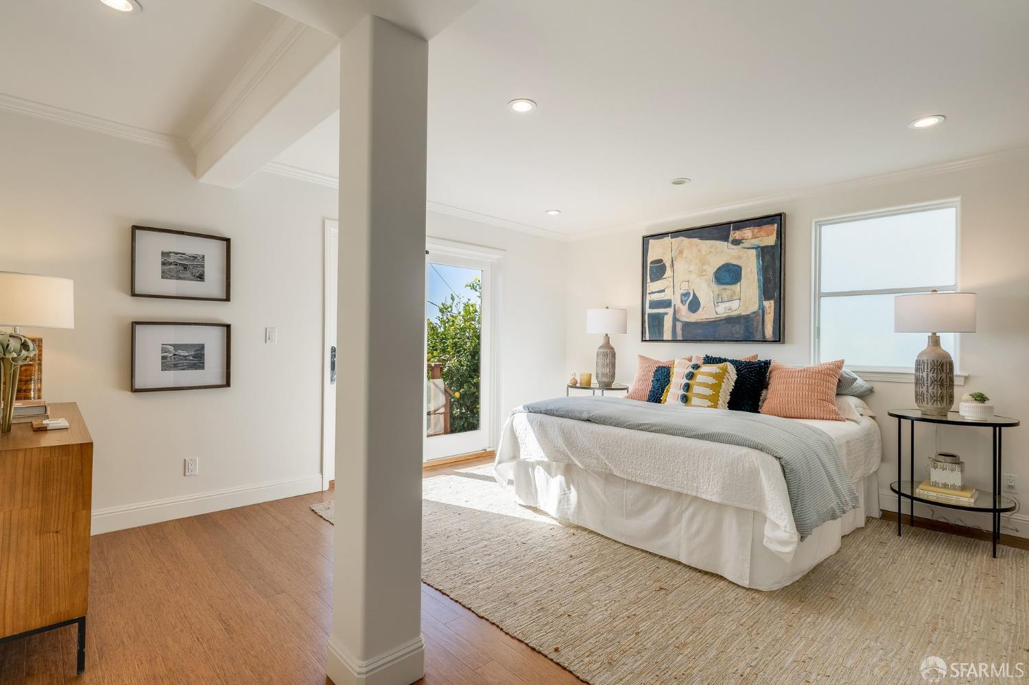 Staged bedroom with a white bed, colorful pillows, and a glass door opening to greenery.