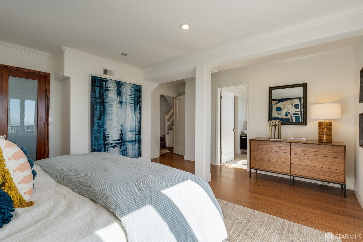 Furnished bedroom with a large bed, blue abstract artwork, and a wooden dresser.