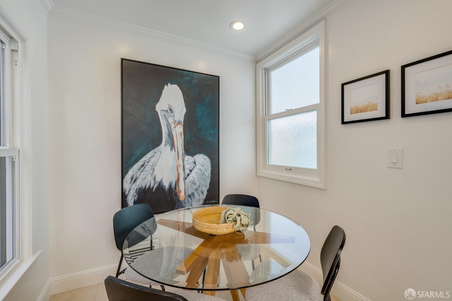 Dining nook with a glass-top table, large windows, and a prominent pelican painting.