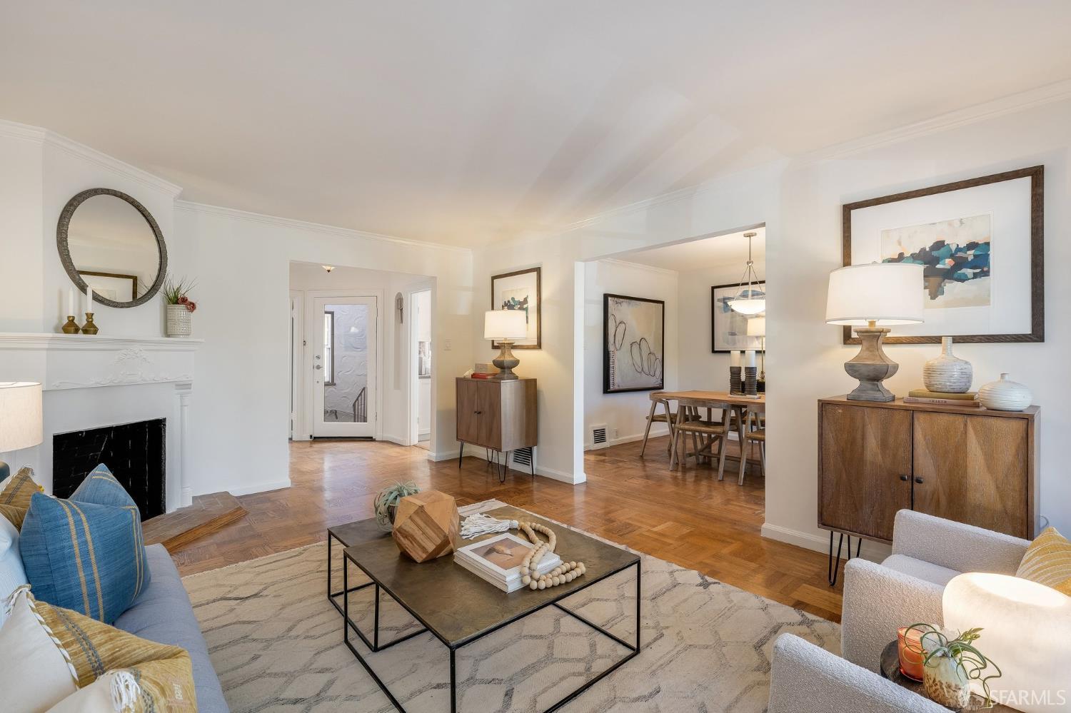Staged living room with a white fireplace, blue sofa, hardwood floors, and adjoining dining area.