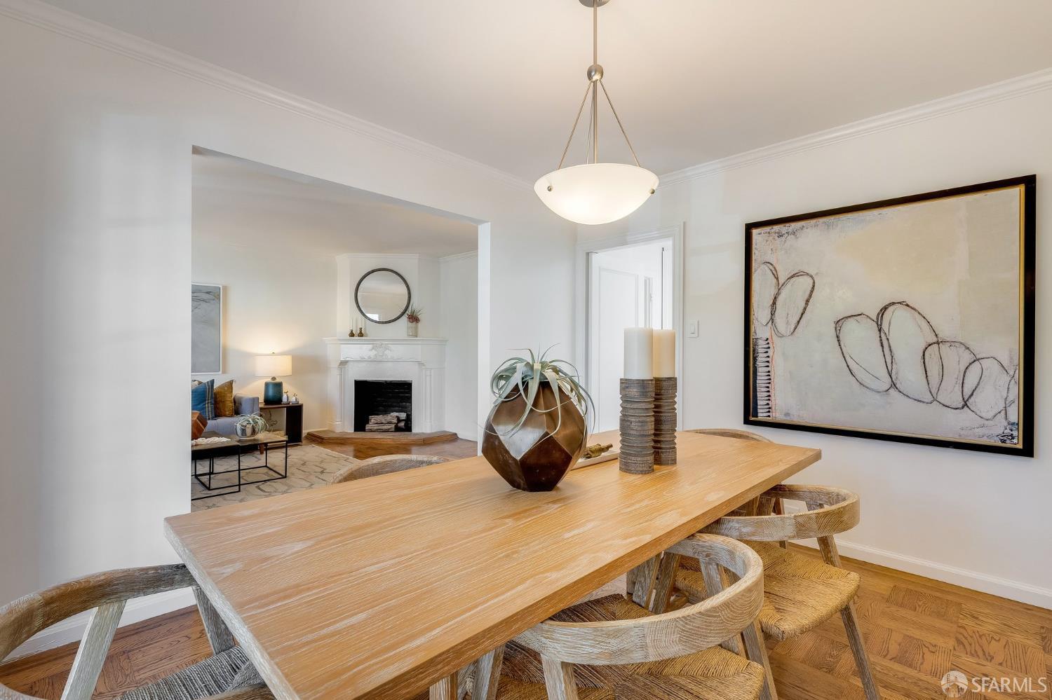 Dining room with a long wooden table and woven chairs, opening to a living room with a white fireplace.