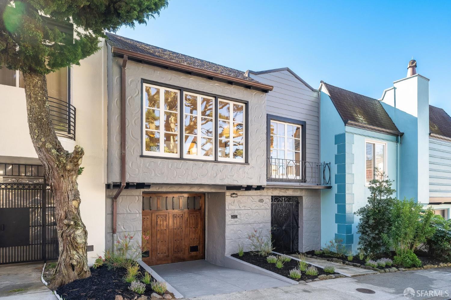 Gray stucco San Francisco home with a wooden garage door, iron entry, and small balcony.