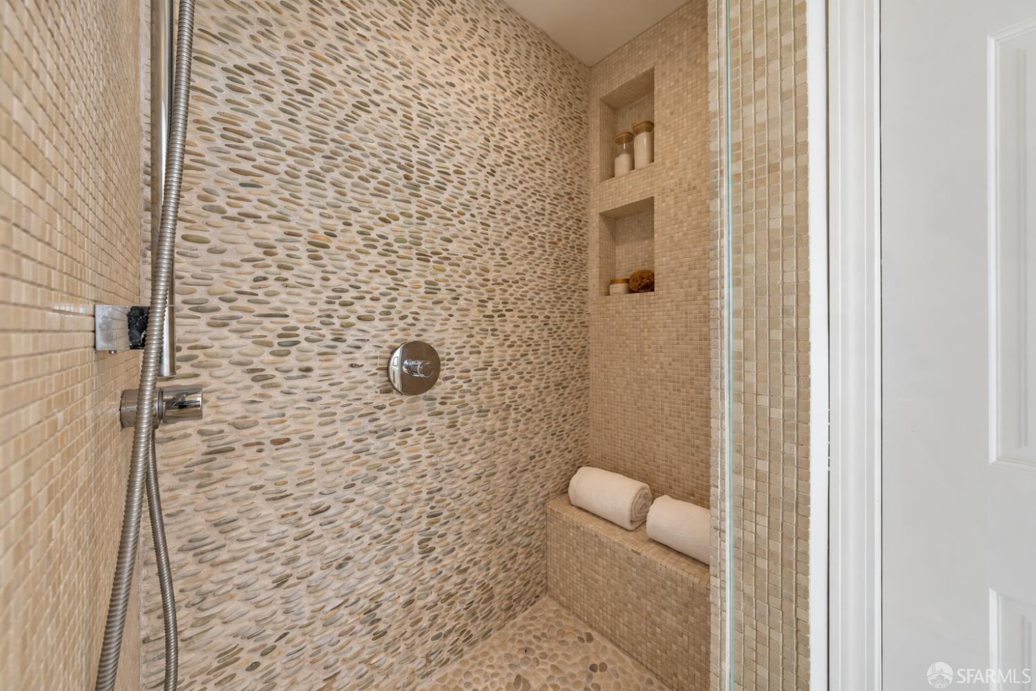 Walk-in shower with a pebble-pattern wall, built-in tiled bench, and recessed niches.