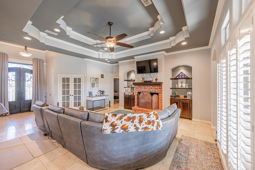 Living room with a brick fireplace, gray sectional sofa, coffered ceiling, and plantation shutters.