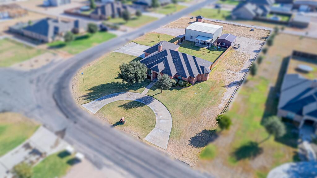 Aerial view of a brick home with a curved driveway and detached metal workshop.