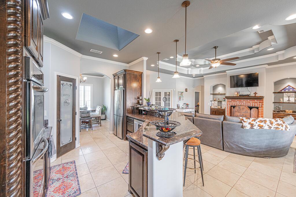 Open-plan kitchen and living area with a granite island, stainless steel appliances, and brick fireplace.