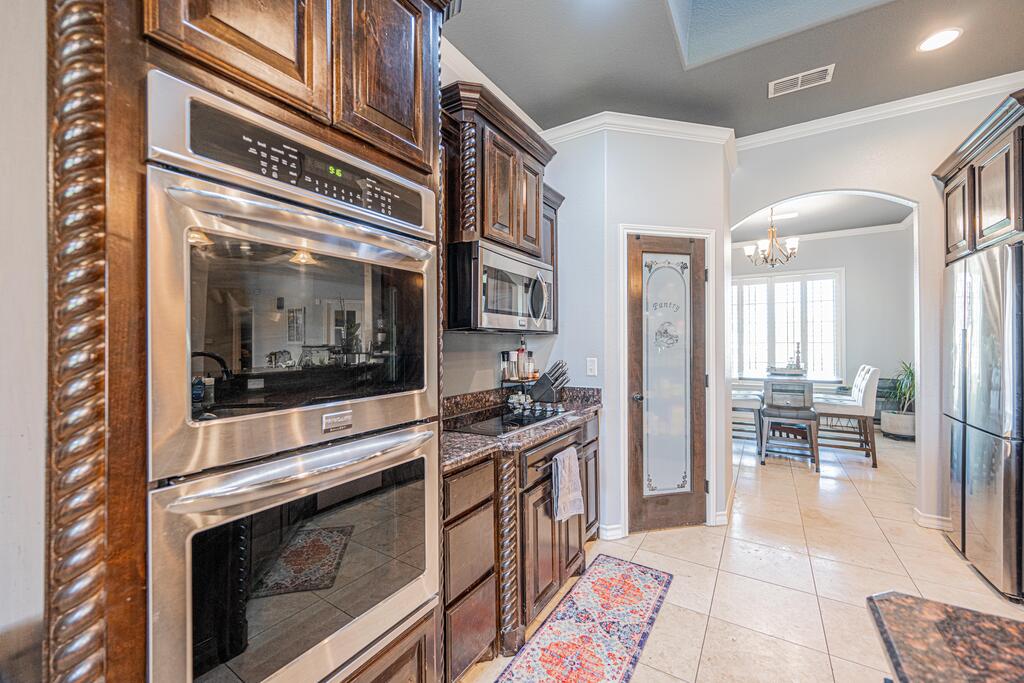 Kitchen with dark wood cabinetry, stacked double ovens, and an arched opening to the dining area.