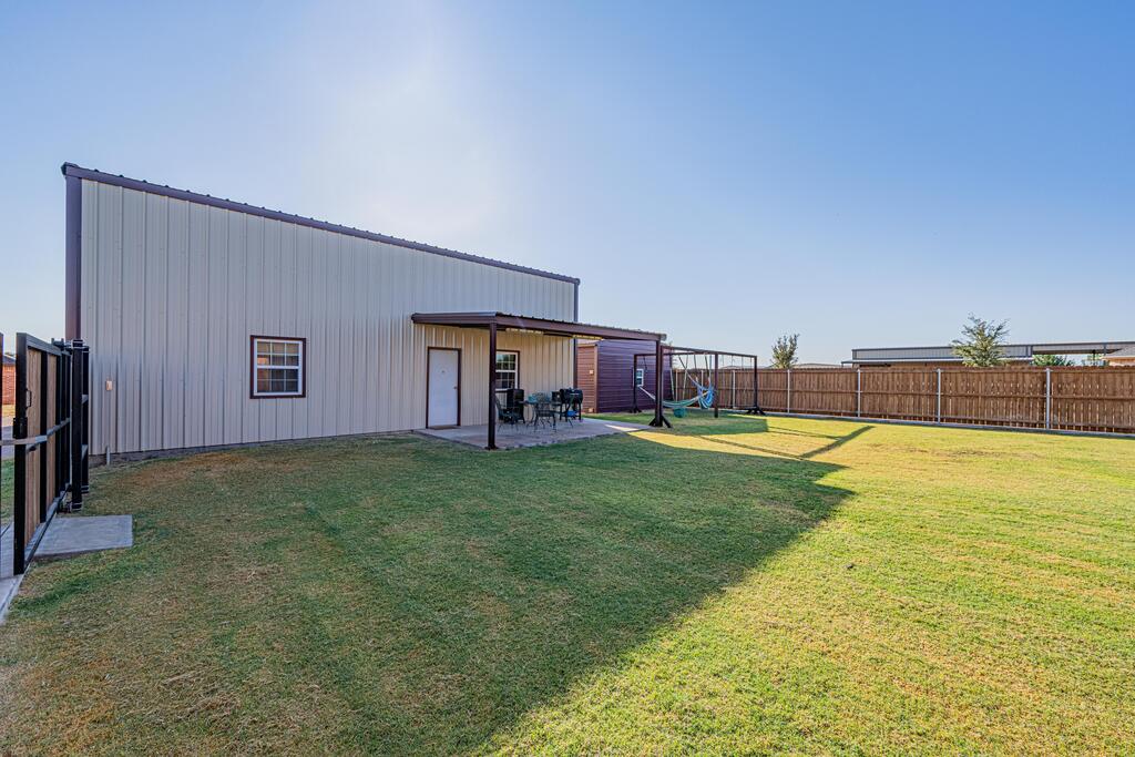 Metal-sided building with a covered patio and fenced lawn.