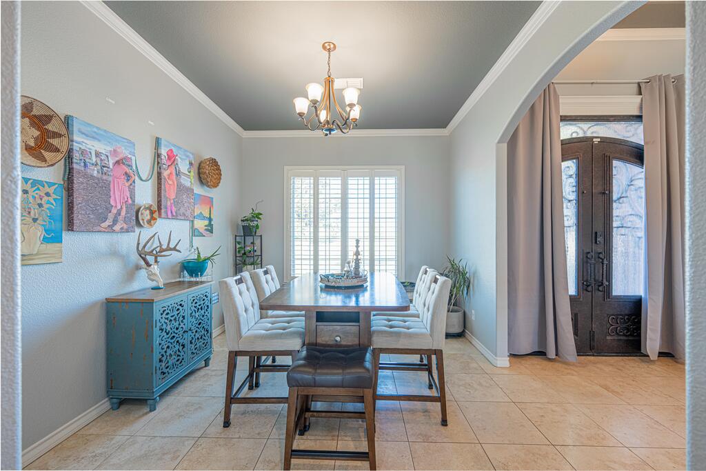Dining room with a wood table, upholstered chairs, chandelier, and arched entry to the front door.