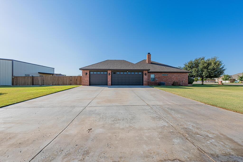 Red brick house with two garage doors, a wide concrete driveway, and a metal outbuilding beside it.