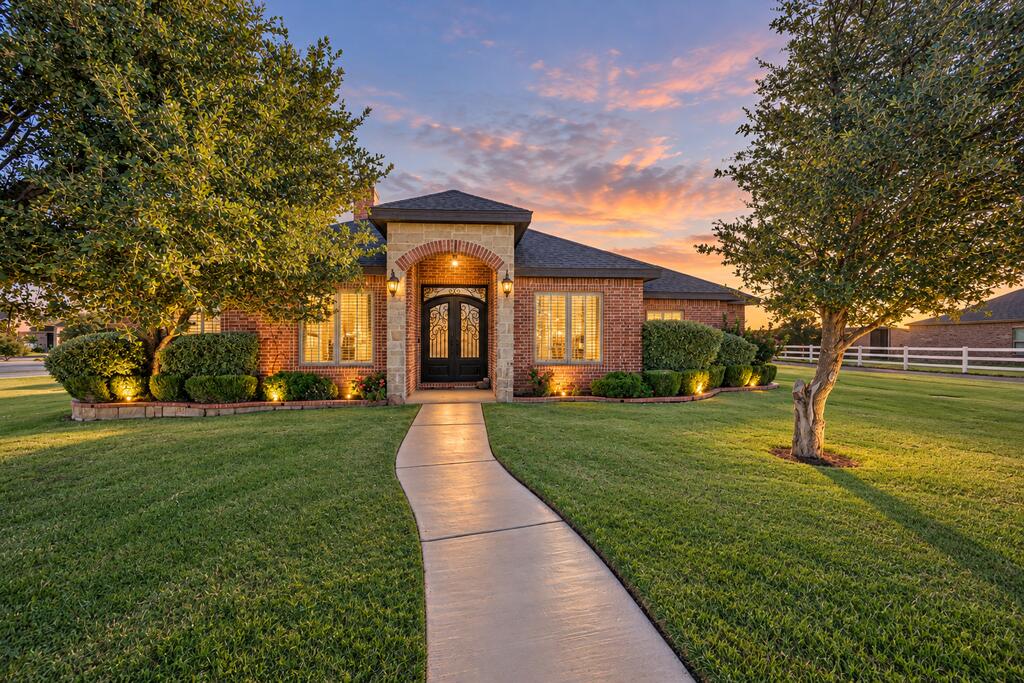 Brick home with an arched entry, landscaped lawn, and curved walkway at dusk.