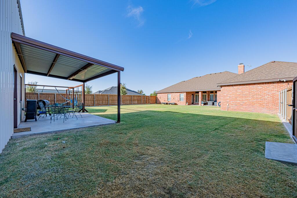 Brick house backyard with a covered patio, outdoor seating, lawn, and wooden privacy fence.