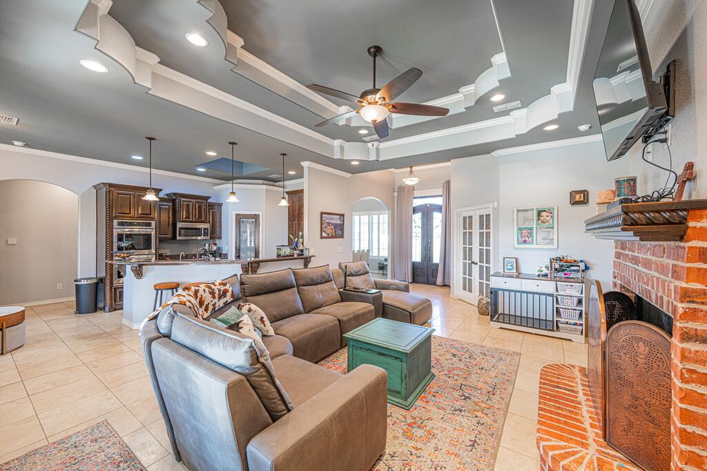 Living room with a large sectional sofa, brick fireplace, and ornate tray ceiling.