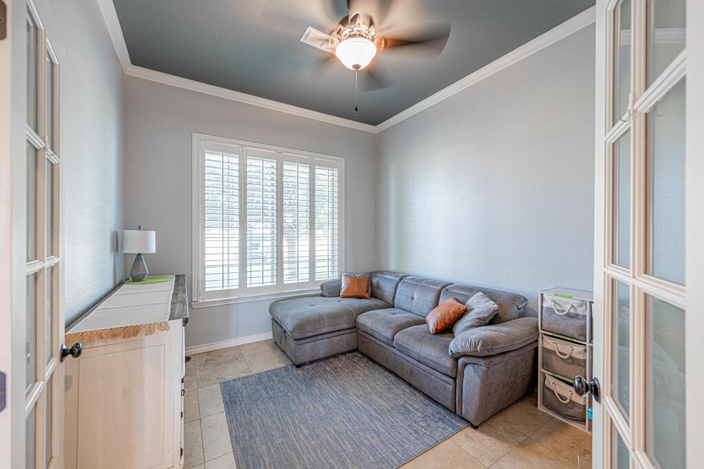 Living room with a gray sectional, plantation shutters, and a ceiling fan beneath a tray ceiling.
