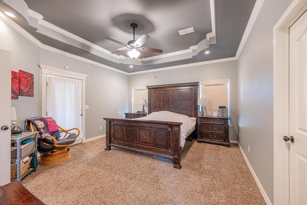 Bedroom with a dark wood bed, tray ceiling, and wicker chair beside a curtained window.