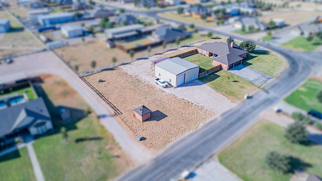 Aerial view of a brick house, detached metal workshop, and fenced lot beside a paved road.
