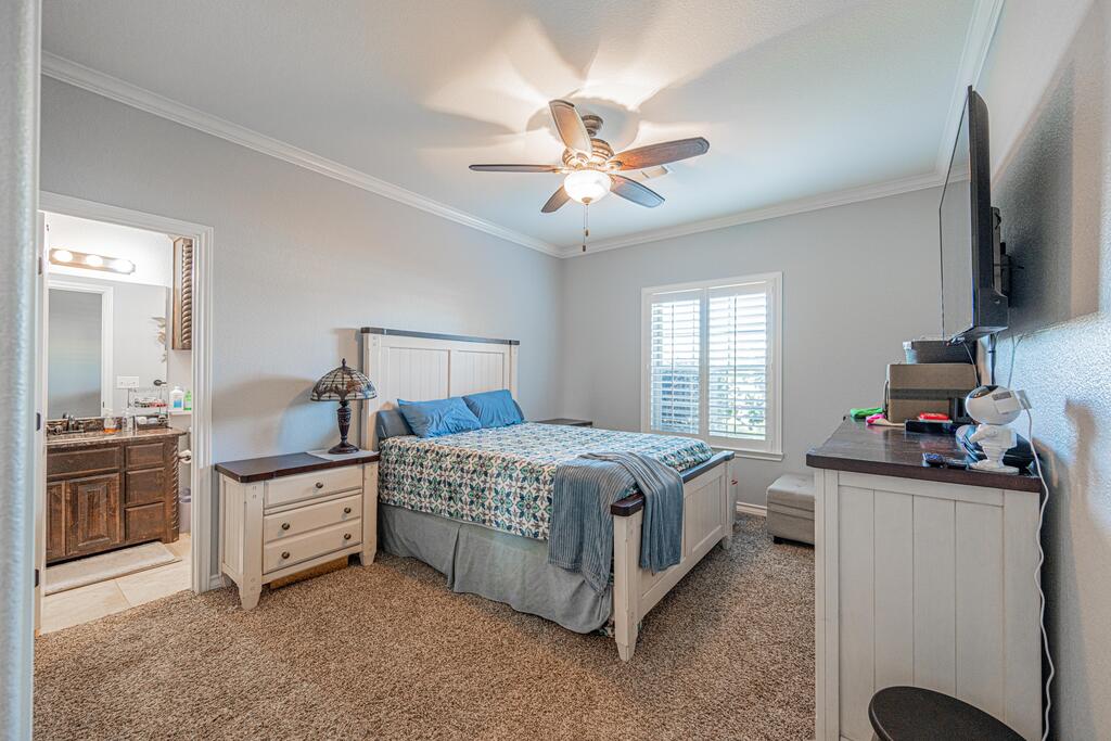 Bedroom with a white bed, blue pillows, patterned bedding, and a ceiling fan beside a shuttered window.
