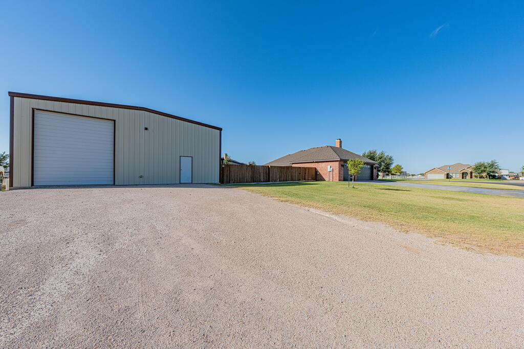 Metal workshop with an oversized roll-up door beside a brick house and gravel driveway.