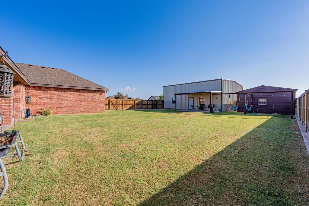 Fenced backyard with a broad lawn, large metal outbuilding, and smaller shed.