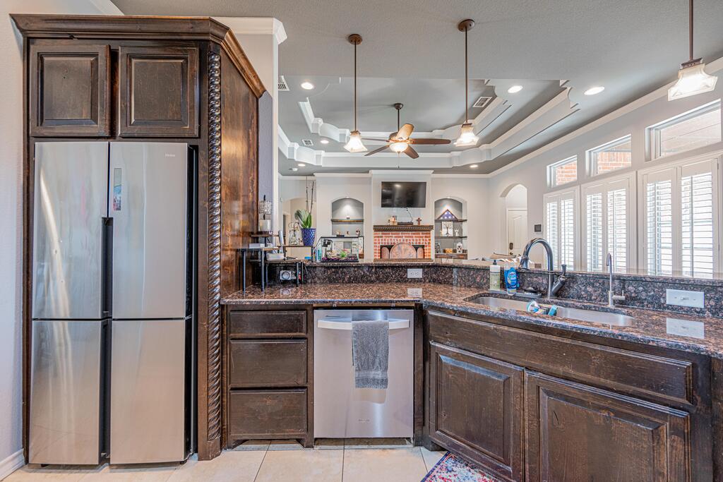 Kitchen with dark wood cabinetry, granite counters, stainless appliances, and shuttered windows above the sink.