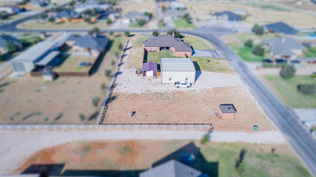 Aerial view of a fenced property with a brick house, large metal outbuilding, and dry yard.