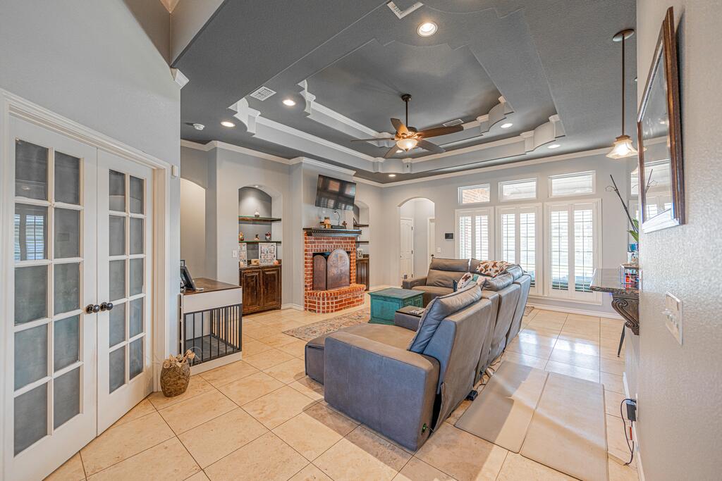 Living room with a gray sectional, brick fireplace, shuttered windows, and tray ceiling.