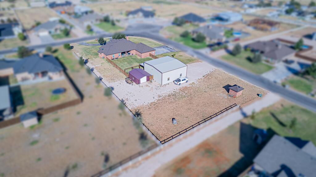 Fenced property with a brick house, large metal outbuilding, and small shed.