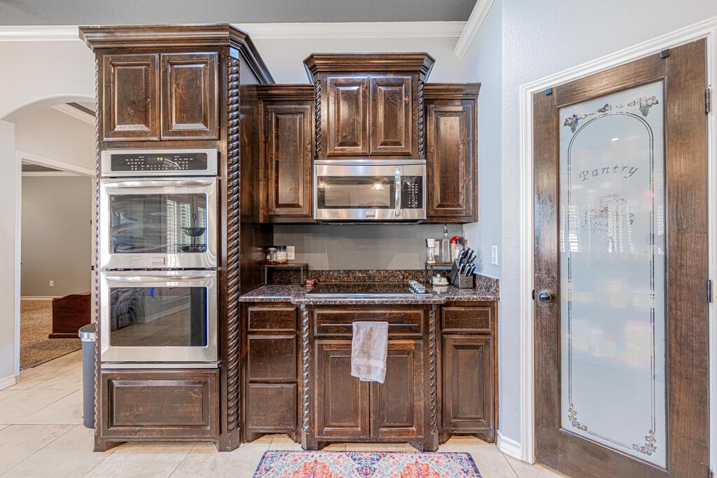 Kitchen with ornate dark wood cabinetry, built-in double oven, and glass-paneled pantry door.