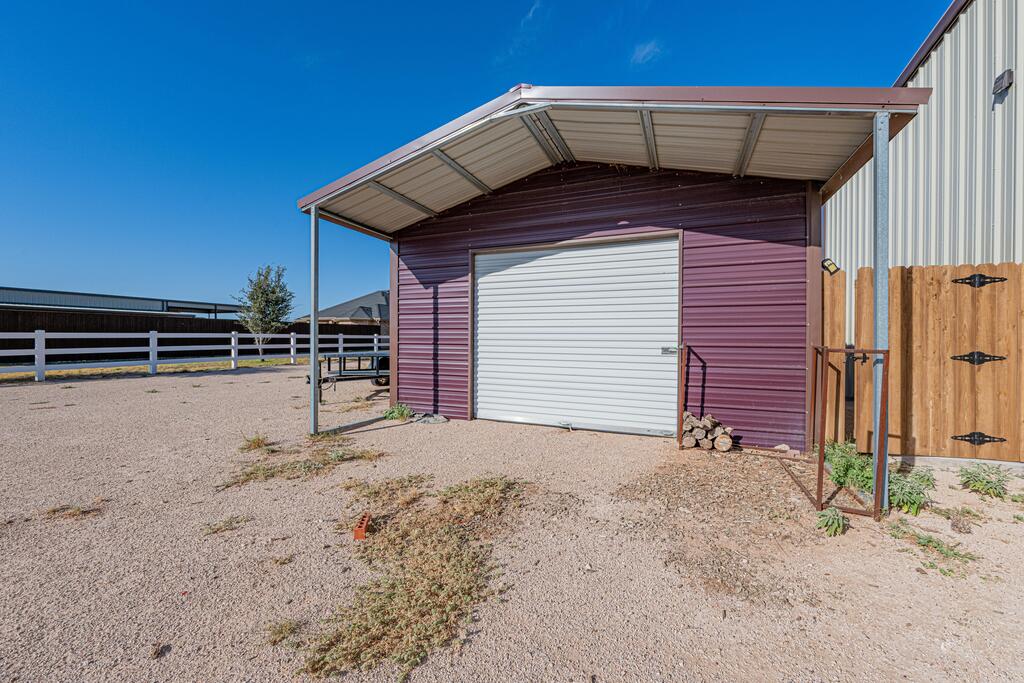 Purple metal-sided outbuilding with a white roll-up door, covered canopy, and wooden gate.