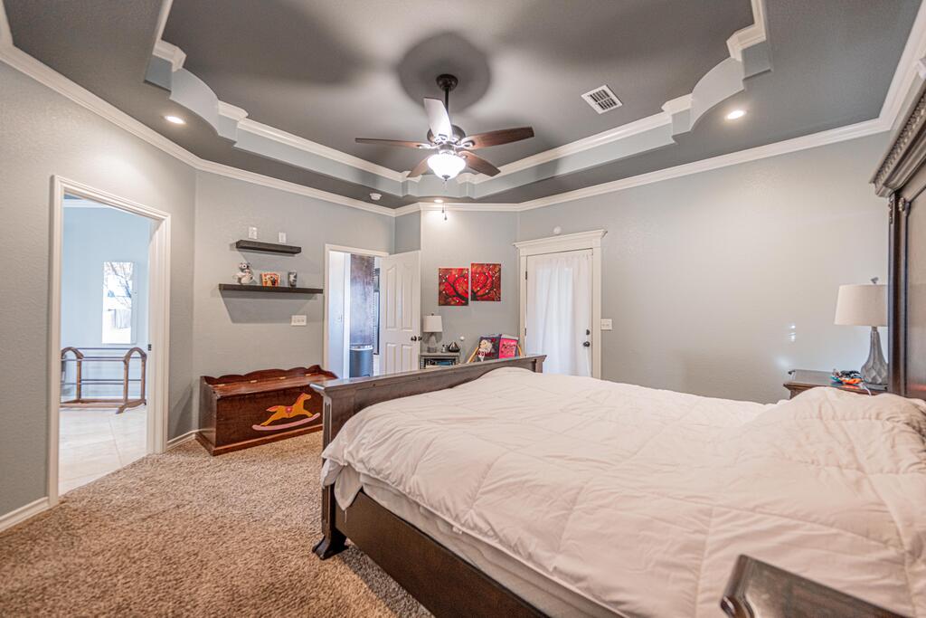 Furnished bedroom with a large bed, patterned tray ceiling, and ceiling fan.