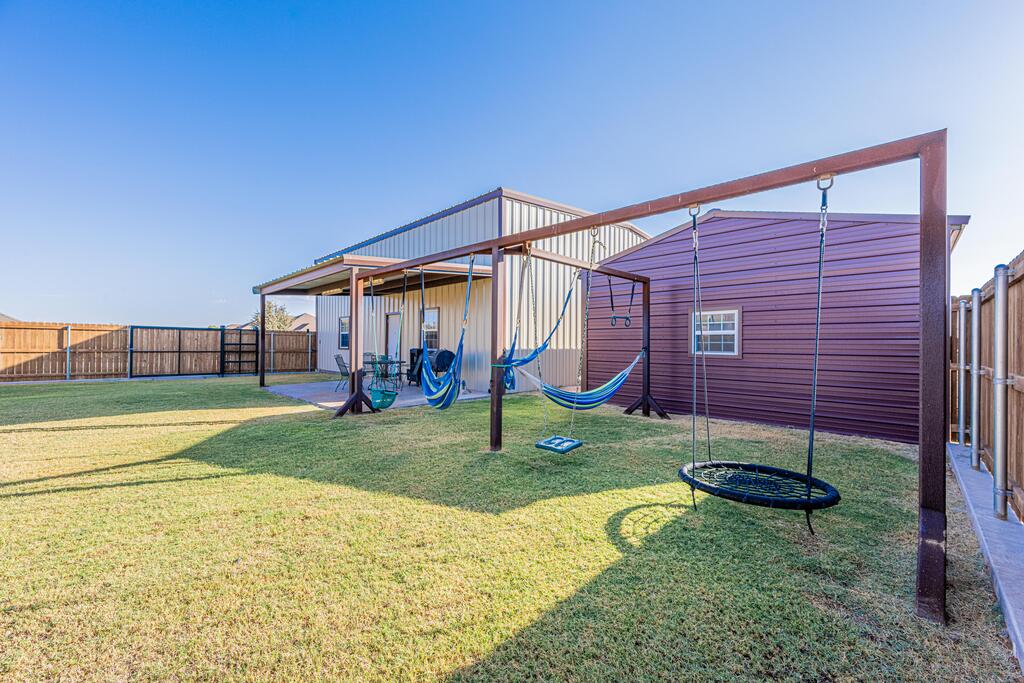 Fenced backyard with a large swing frame, hammocks, lawn, and metal-sided outbuildings.