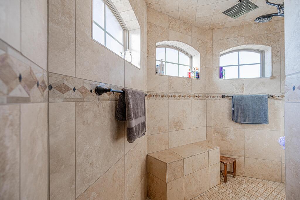 Walk-in shower with a built-in tiled bench, arched windows, and rainfall showerhead.