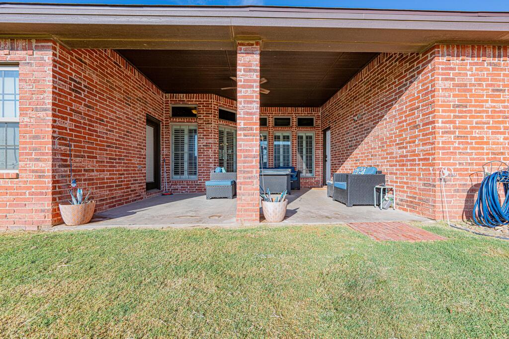 Covered brick patio with outdoor seating and a lawn.