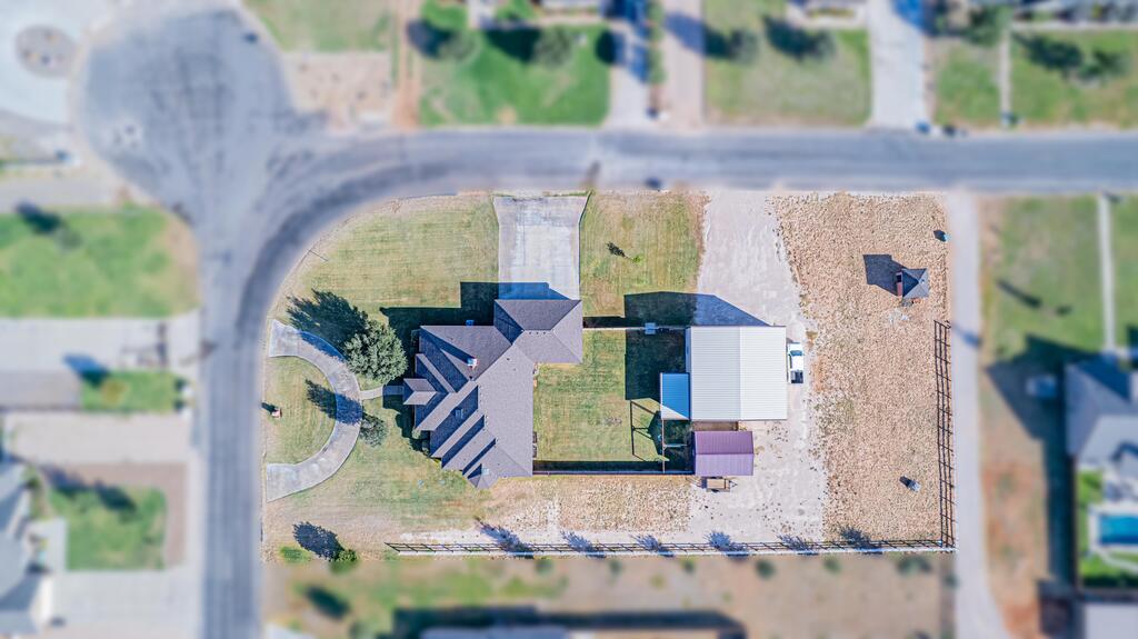 Aerial view of a house and outbuildings on a fenced lot beside a road.
