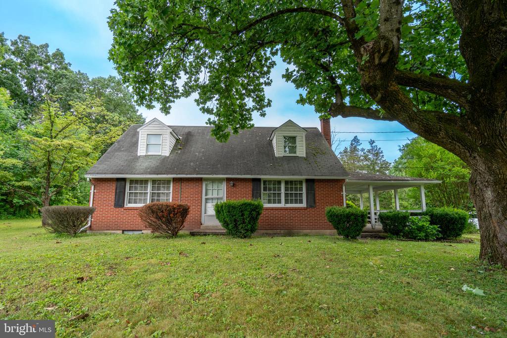 Red-brick house with two dormers, a covered porch, and a large shade tree in the front yard.