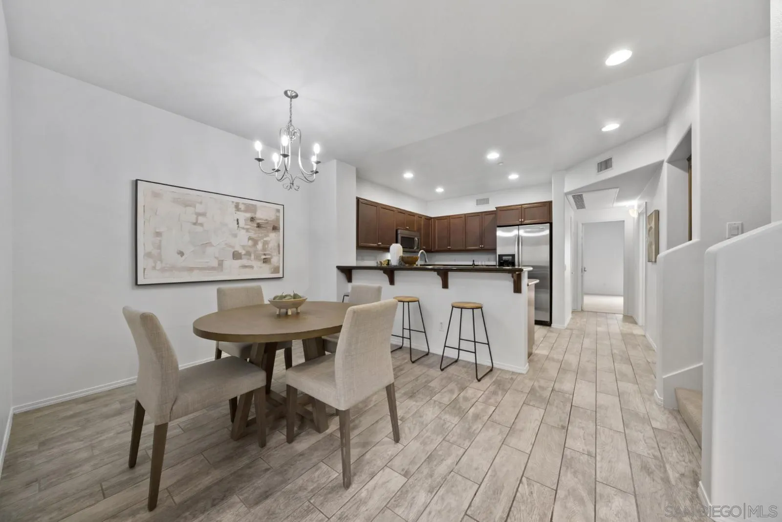 Dining area with a round table and upholstered chairs beside a kitchen with a breakfast bar.
