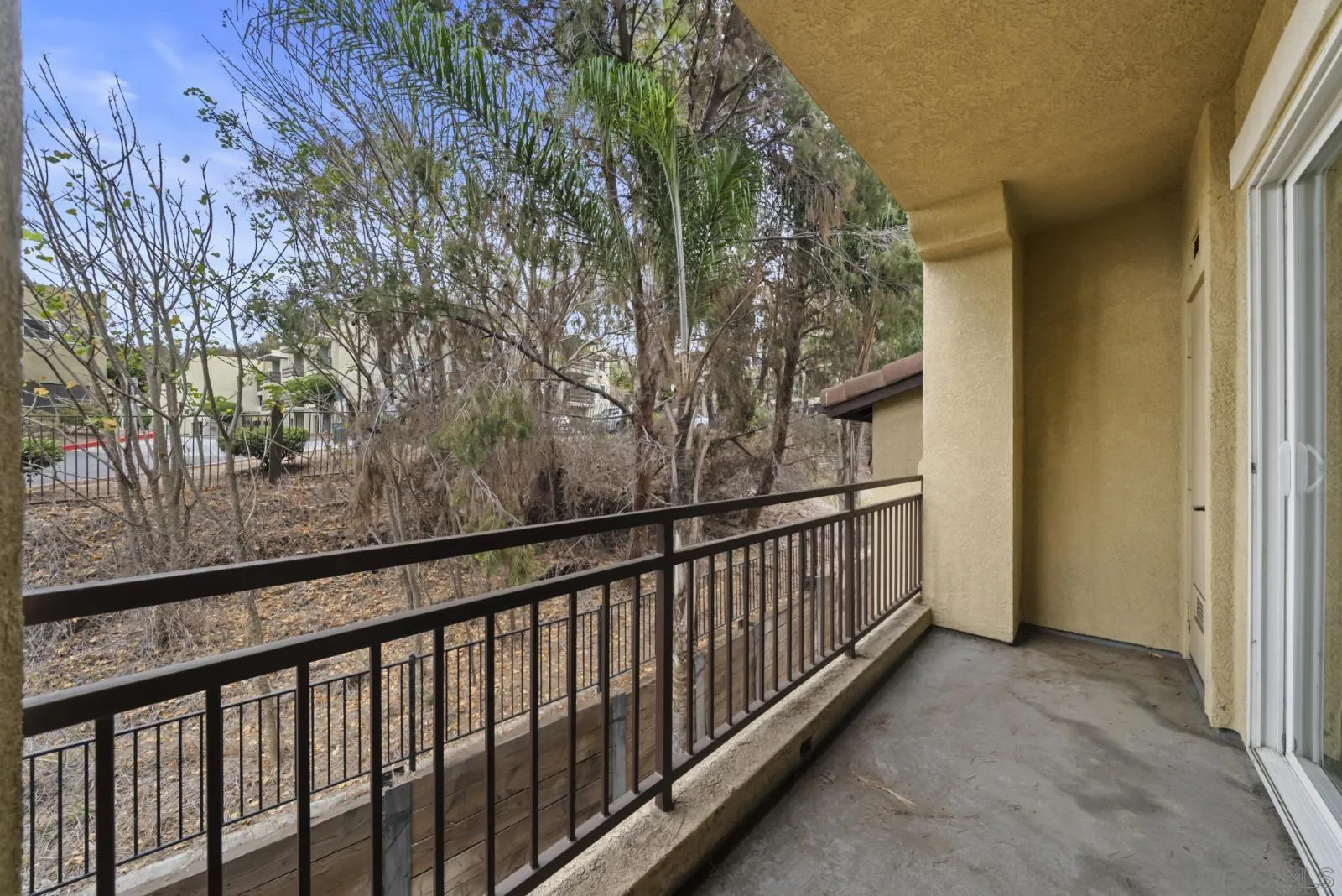 Covered balcony with black metal railing overlooking trees and brush.