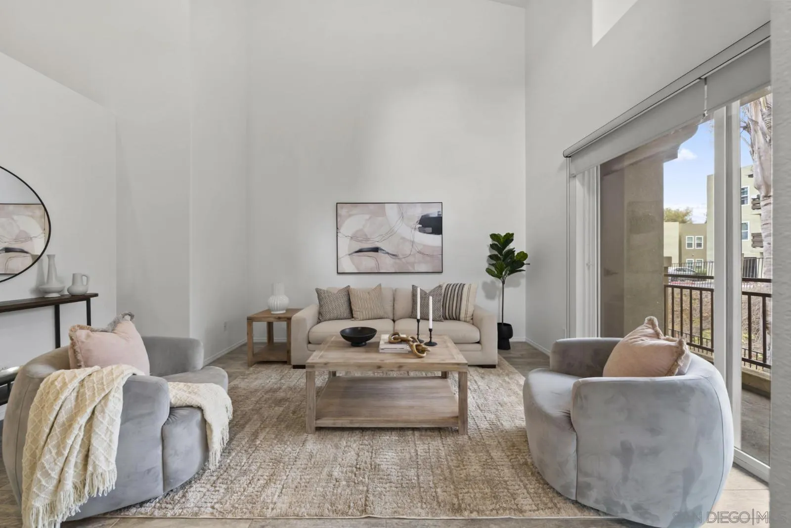Staged living room with a high ceiling, neutral furnishings, and sliding doors to a balcony.